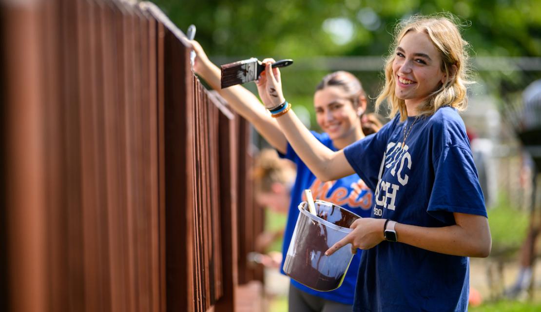 Student volunteers paint a fence as part of Humanics in Action