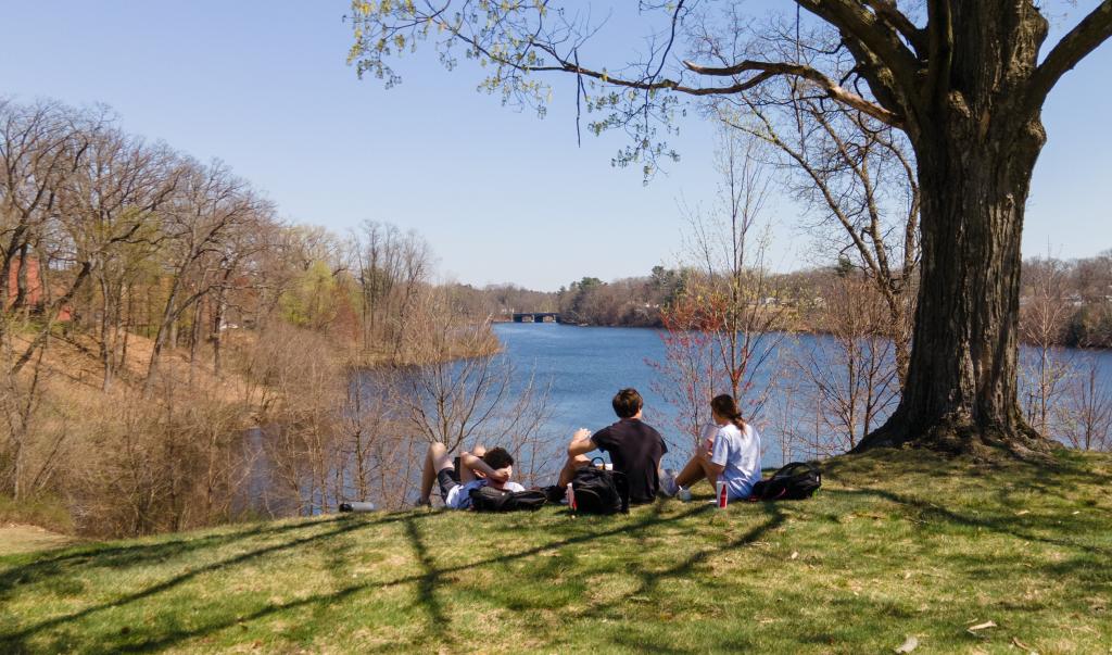 Students relax in the warm sunshine on Rally Hill overlooking Lake Massasoit at Springfield College on Thursday, April 13, 2023.