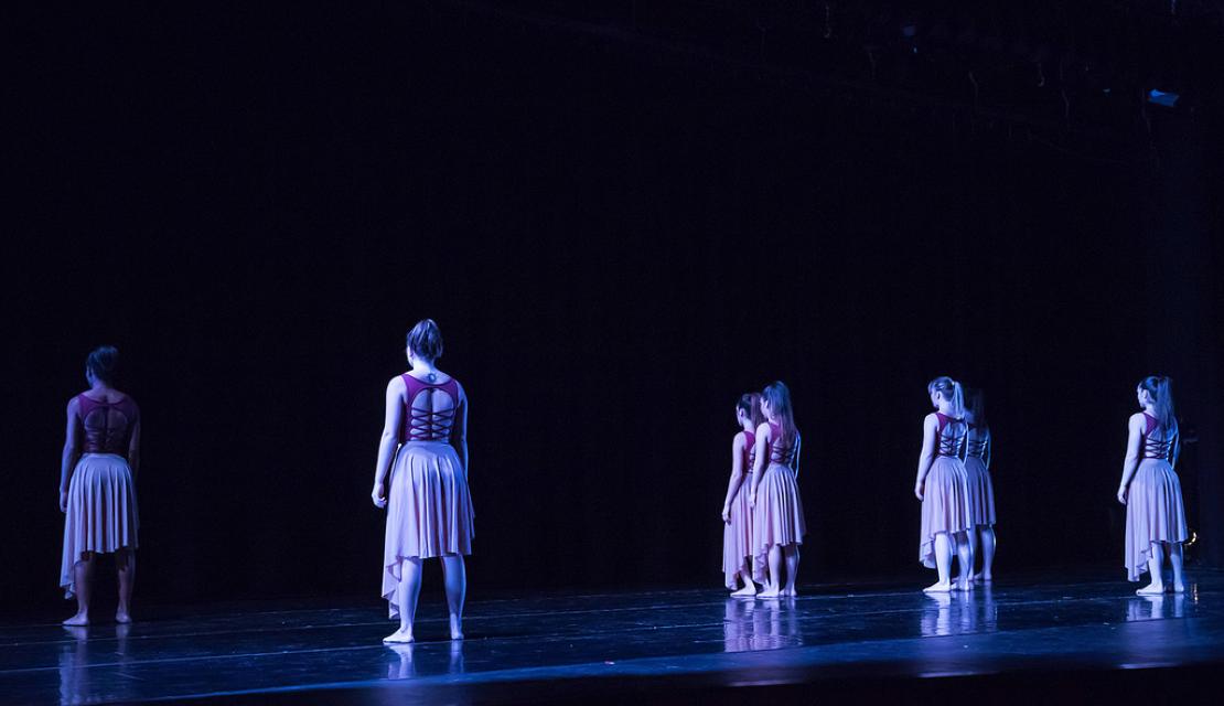Dancers stand on stage with their backs to the audience