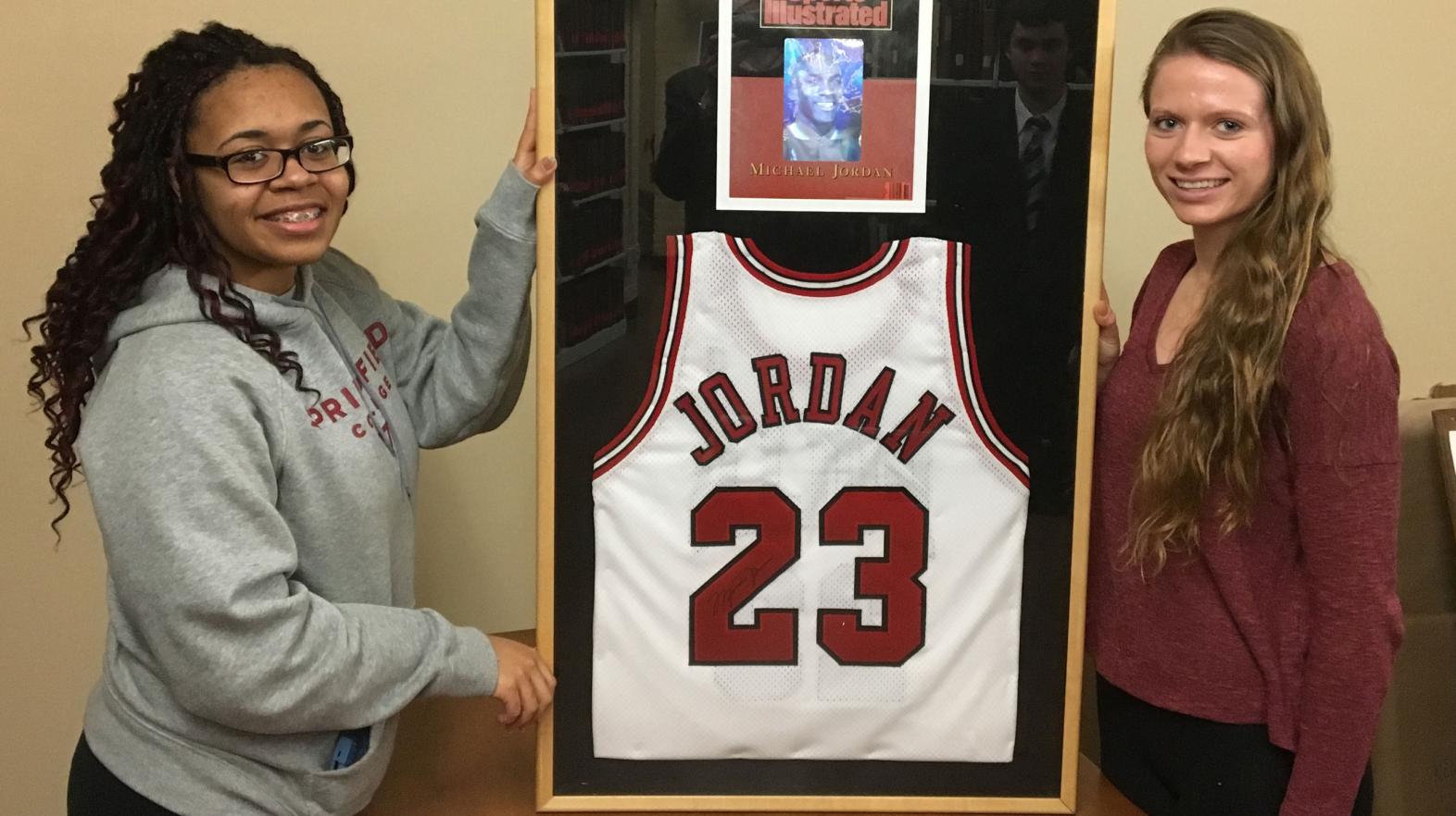 Students pose with a framed Michael Jordan Jersey, located in the Springfield College archives.