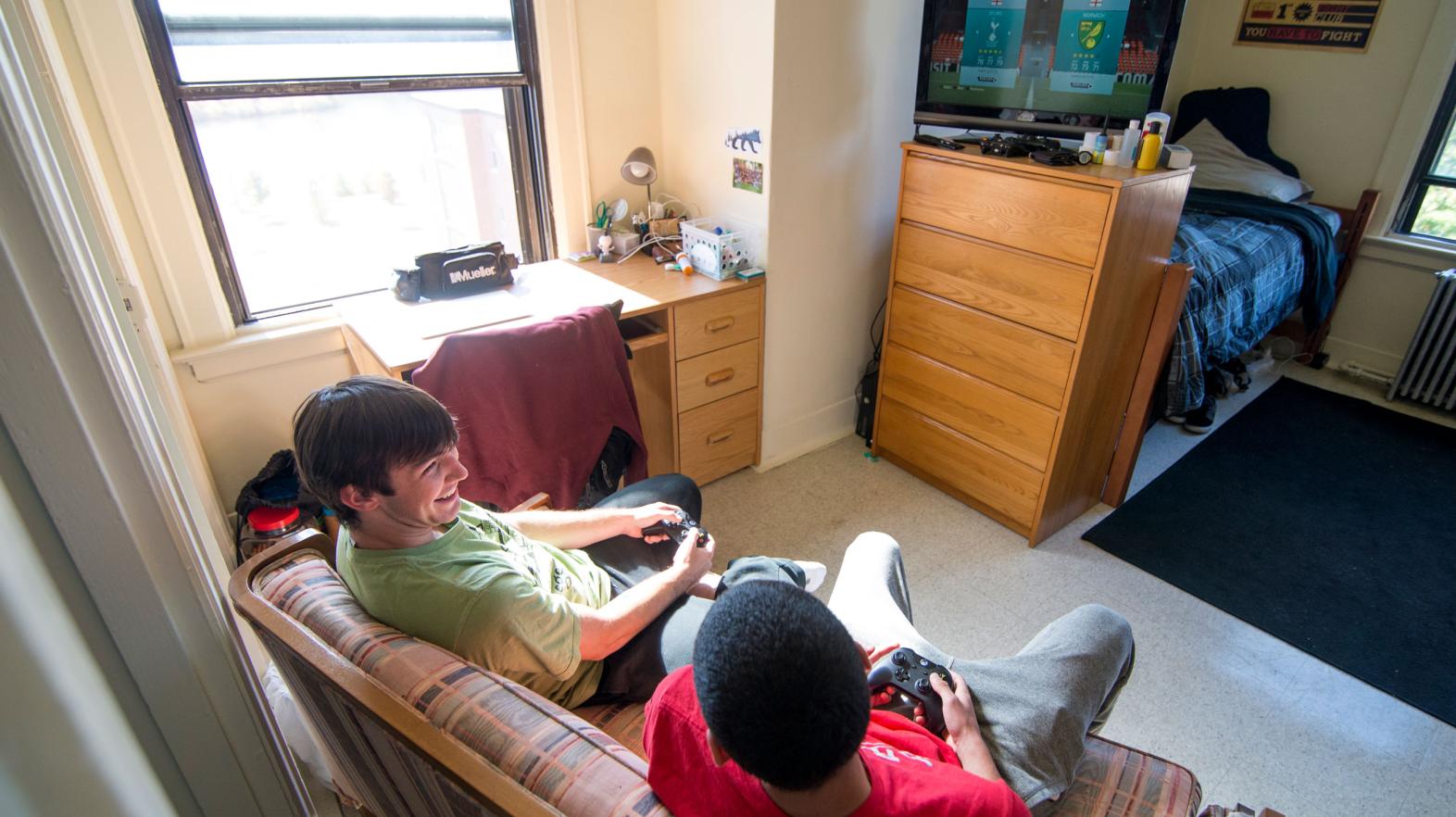 Two students laugh with eachother while playing video games in their residence hall room.