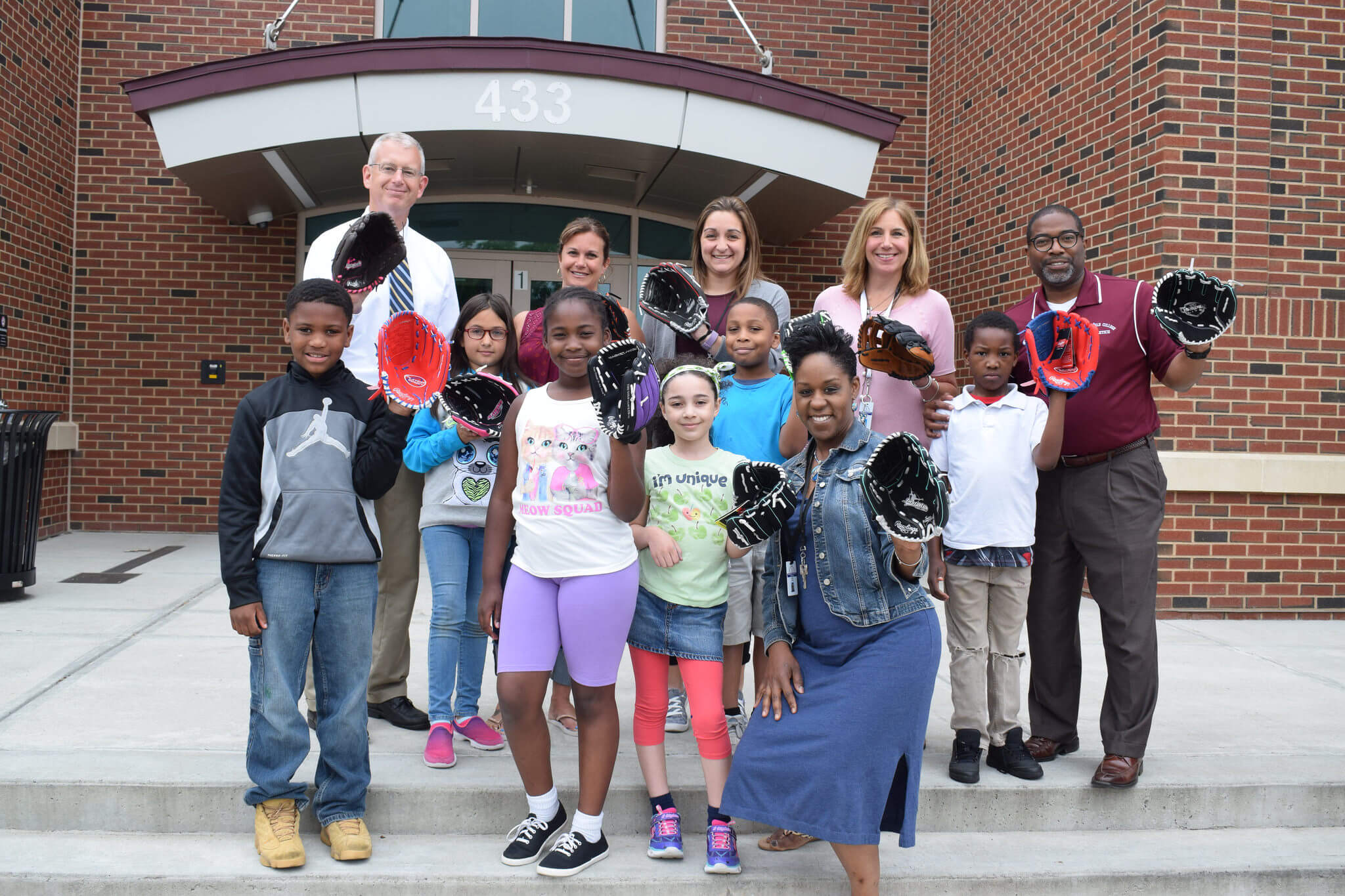 Springfield College staff stand with children on the steps, holding out baseball gloves that were just donated. 