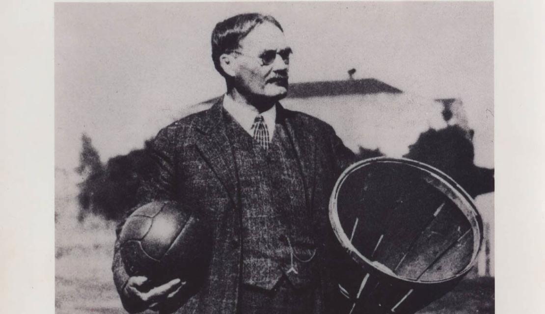 James Naismith holds up a peach basket and basketball during the games early years at Springfield College.