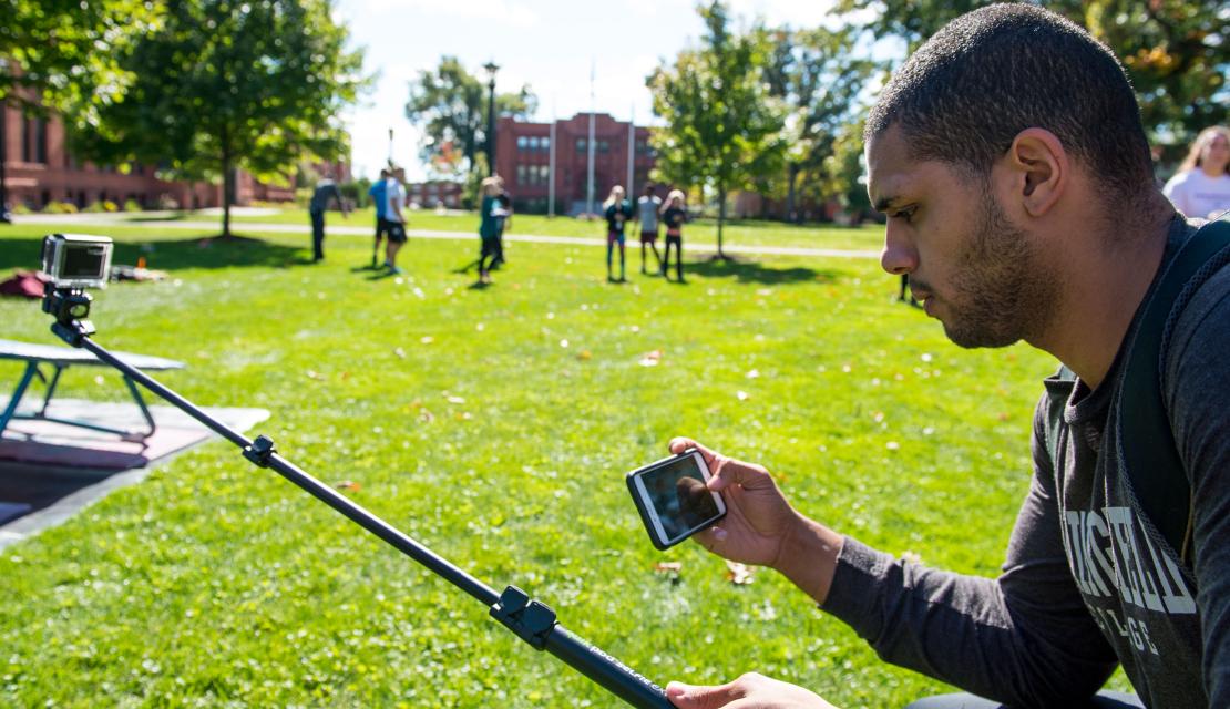 A student looks at his phone as he works on a project on the campus green.