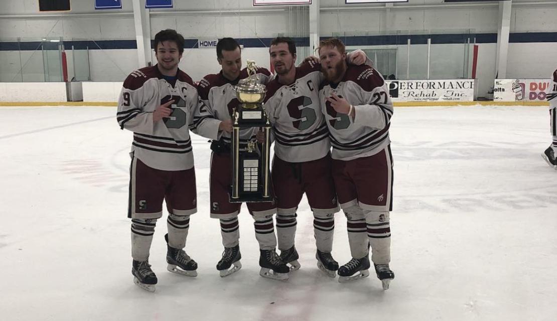 Members of the ice hockey club sport hold a trophy on the ice. 