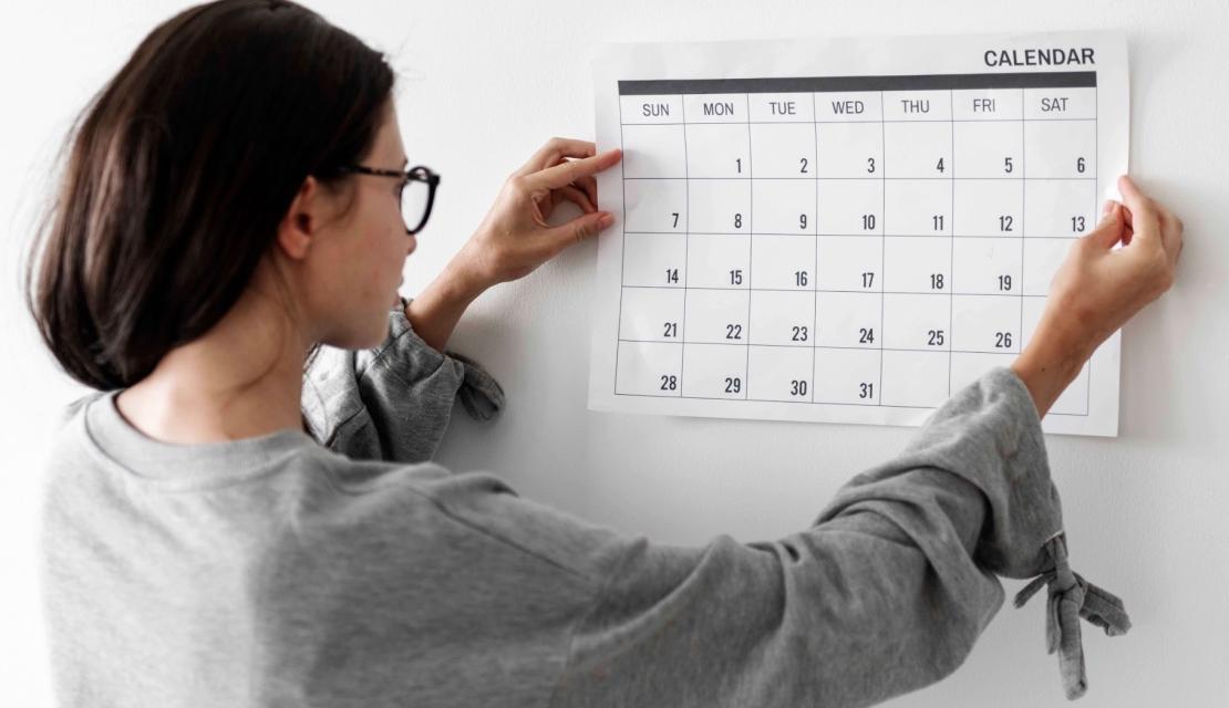 A woman hangs a calendar on the wall. 