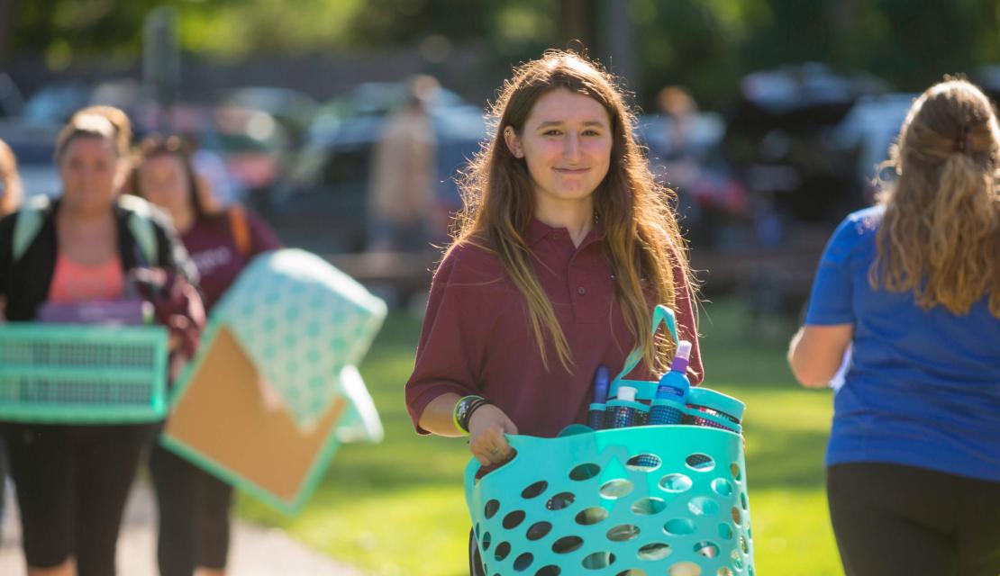A girl moving into a residence hall holds a basket. 