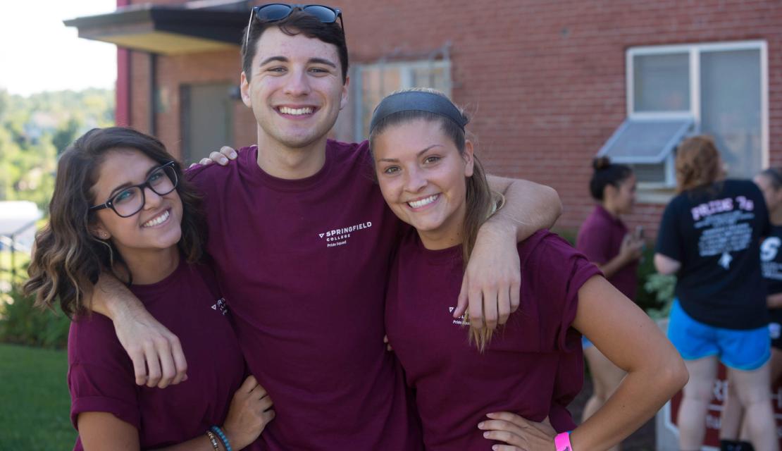 Three students with their arms around each other outside of a residence hall. 