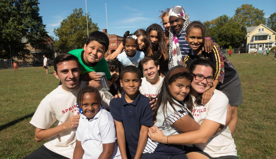 Springfield College students pose on the playground with the students they are volunteering with. 