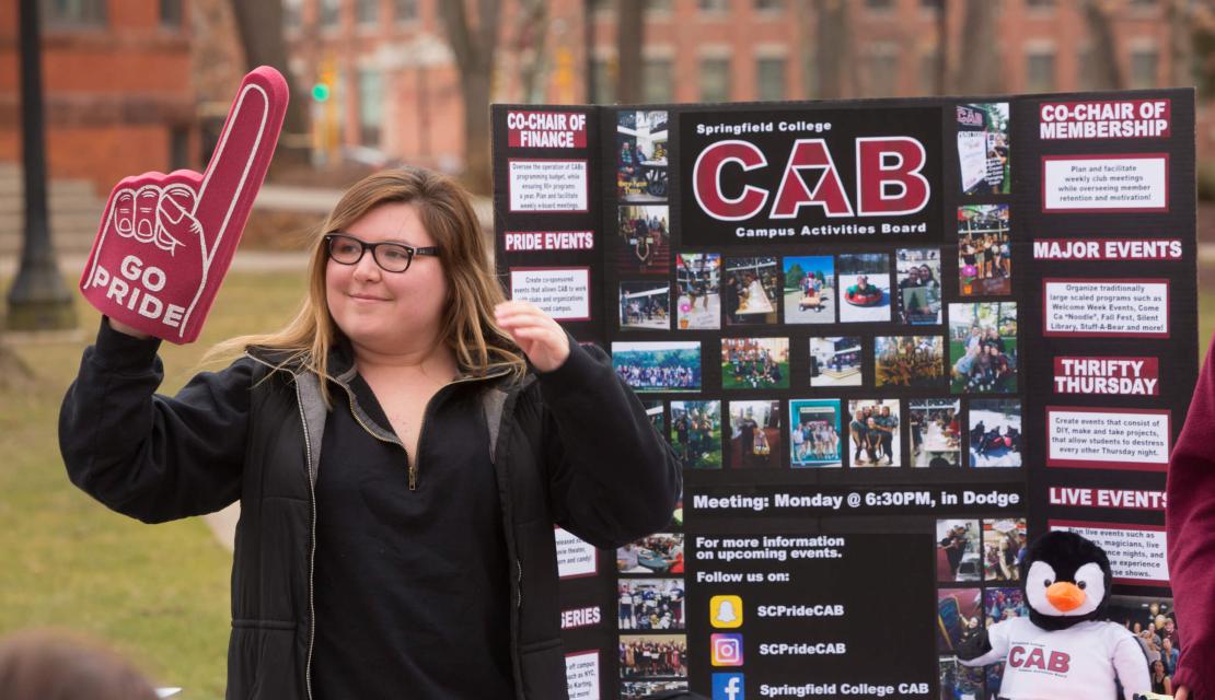 A student stands by a poster promoting an on campus club. 