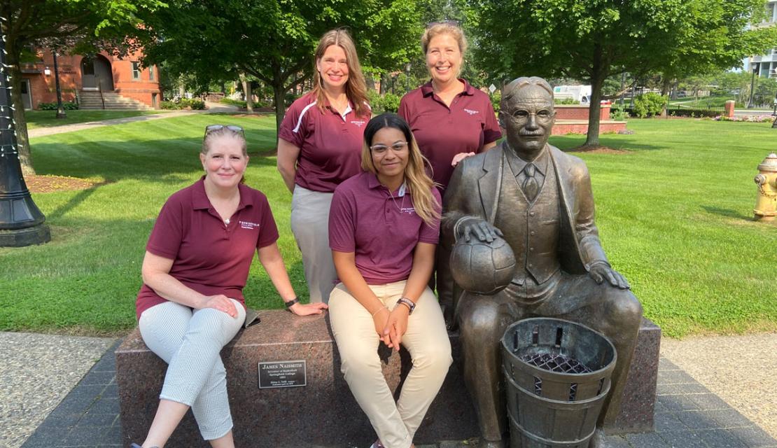 Alumni Relations staff from Springfield College pose with the statue of James Naismith on the Naismith Green