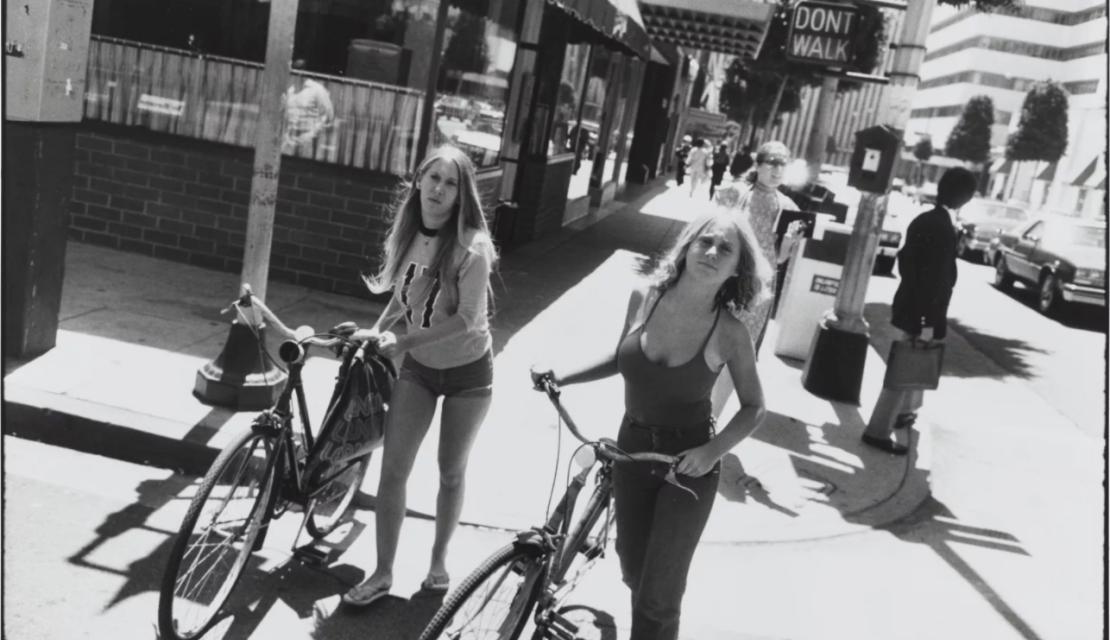 Black and white photo of people walking bicycles. 