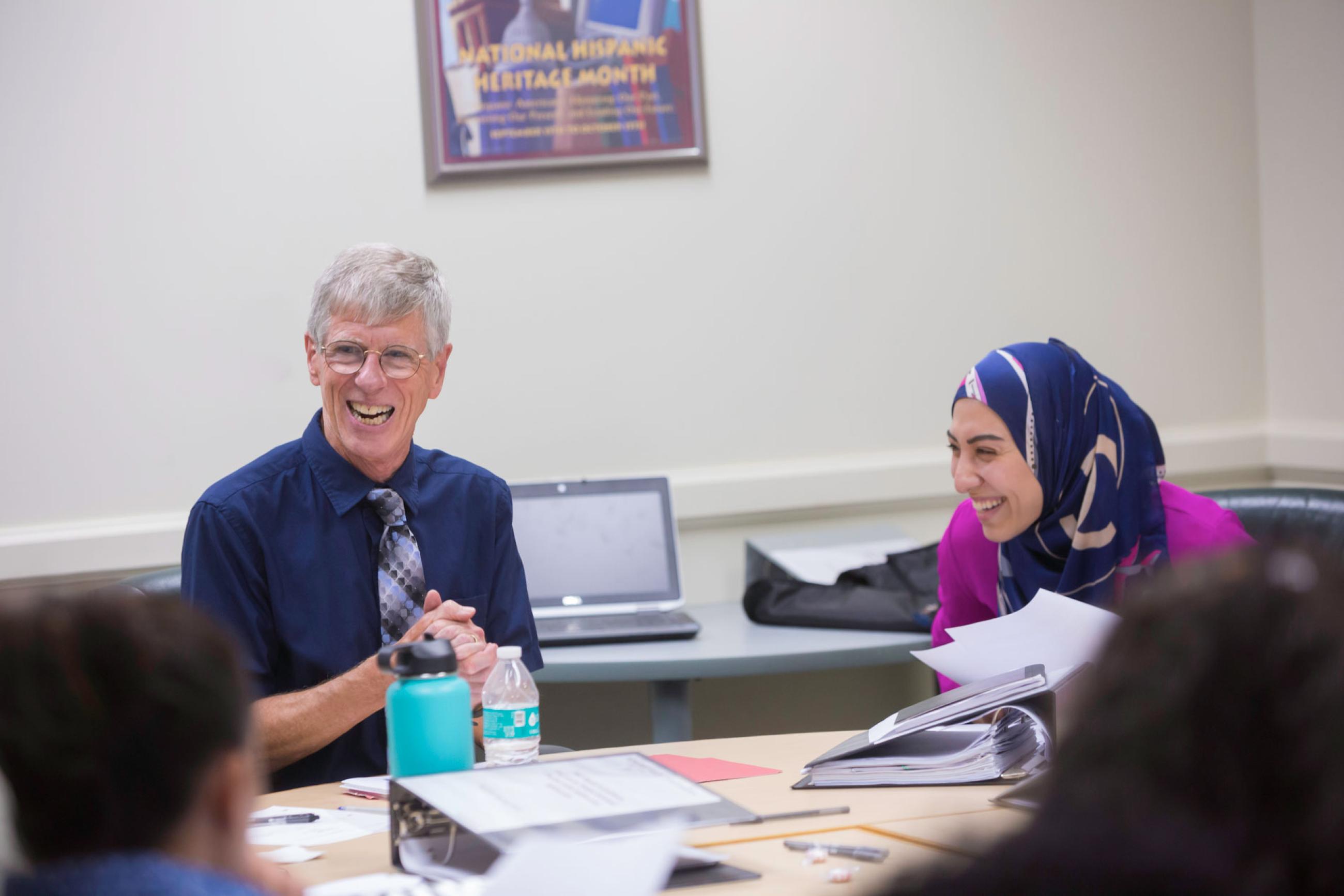 Faculty Walter Mullin laughs alongside a student in a classroom setting