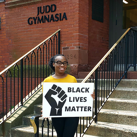 student holding BLM sign in front of Judd Gymnasia