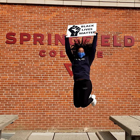 student jumping with Black Lives Matter sign in front of Springfield College sign