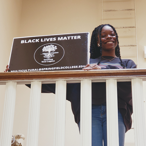 student in tent on stairs holding Black Lives Matter sign