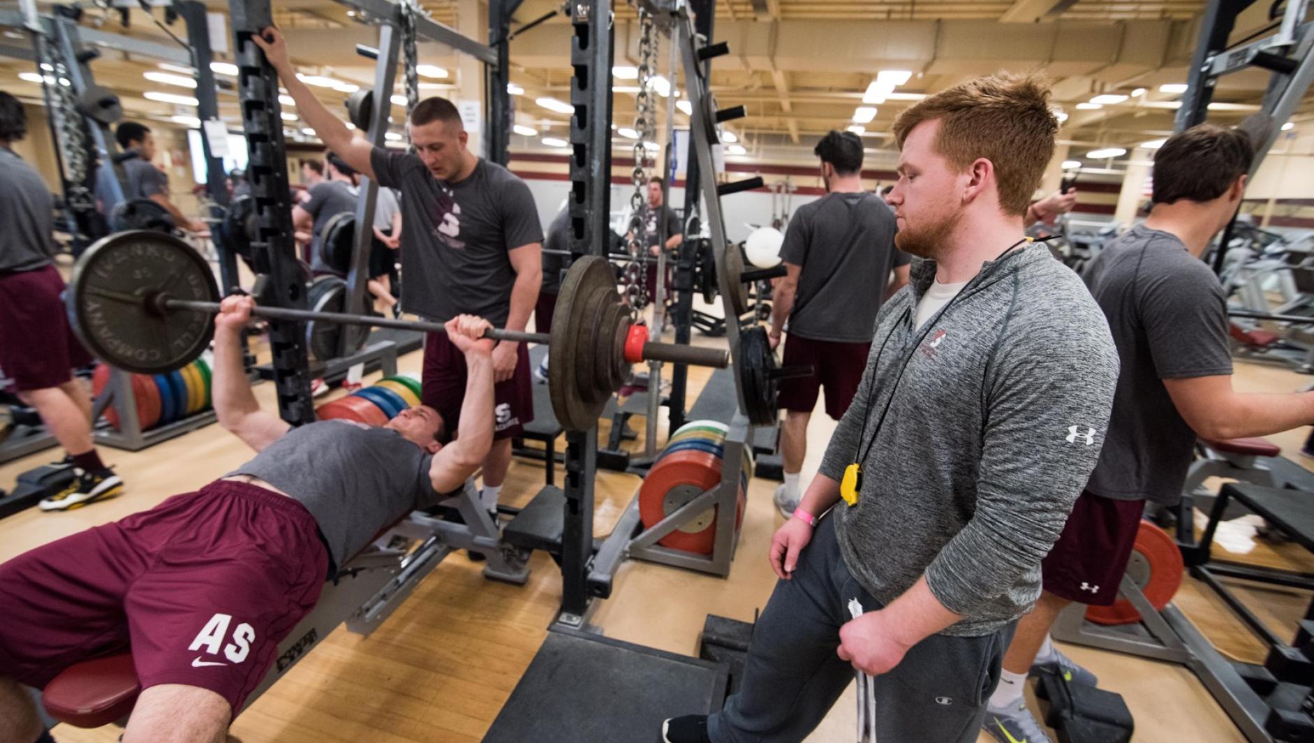A student strength and conditioning coach looks on as his client does a chest press.