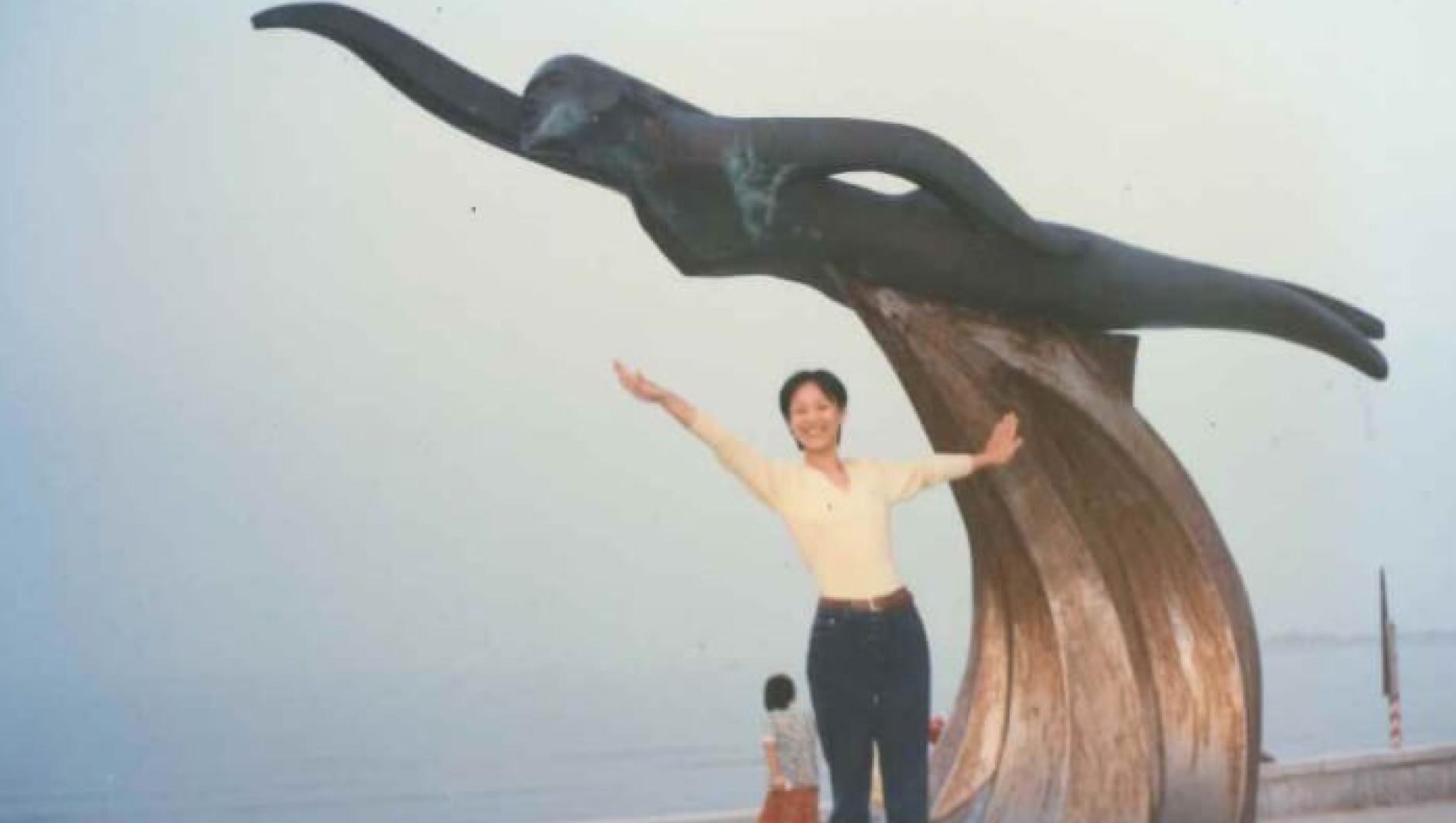Li Jin poses on a statue of a wave. 