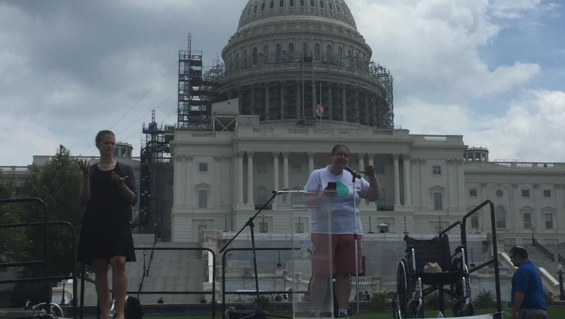 Sarah gives a speech in front of a capital building. 