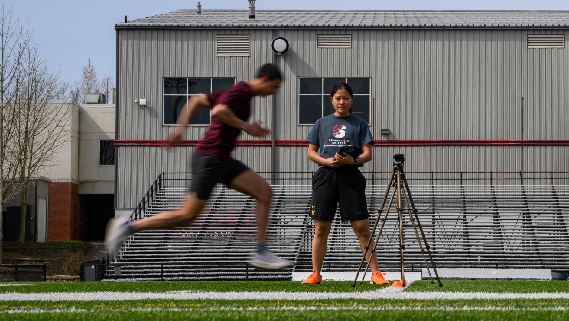 Graduate students enrolled in the Springfield College Strength and Conditioning masters program study with student athletes outside on Stagg Field 