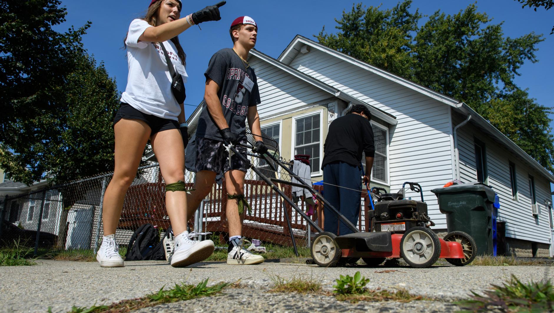 Male and female student pushing a lawnmower in Springfield neighborhood