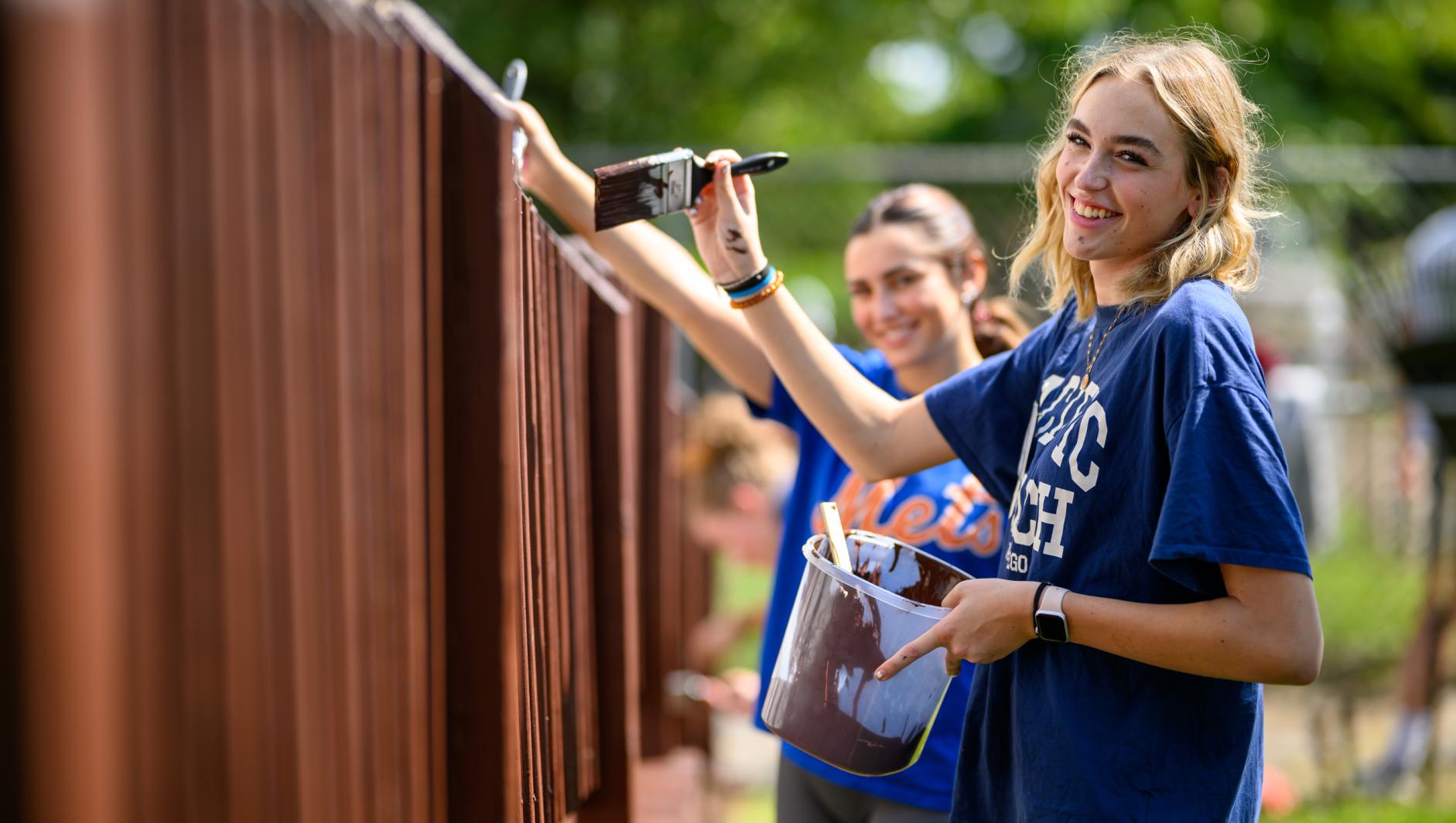 Female student painting fence on humanics in action day