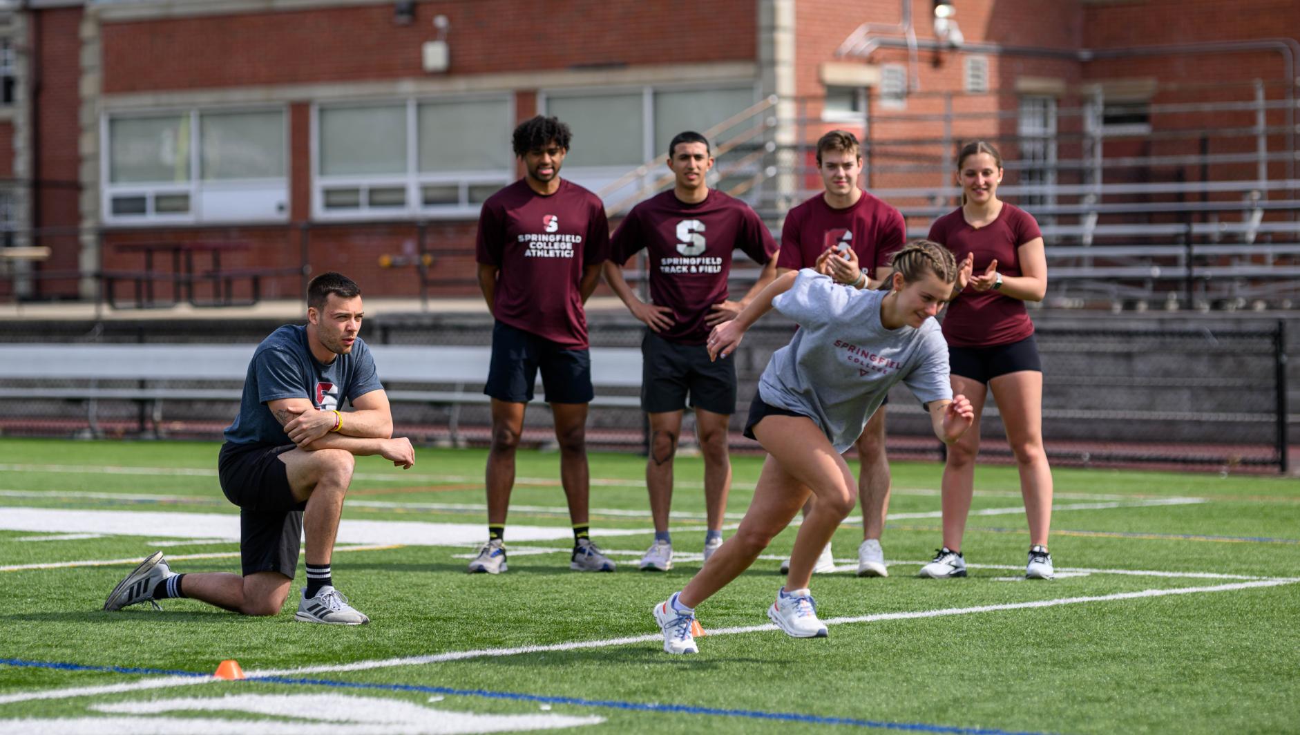 Graduate students enrolled in the Springfield College Strength and Conditioning masters program study with student athletes outside on Stagg Field on April 10, 2024