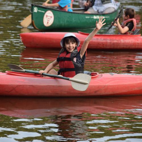 A girl wave from her kayak on Lake Massasoit while attending camp. 