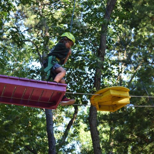 A camper climbs above in the tree in the ropes course at Camp Massasoit. 