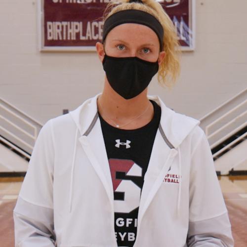 Camryn Bancroft, wearing a mask, is standing on the volleyball court in Blake Arena holding a volleyball in front of her