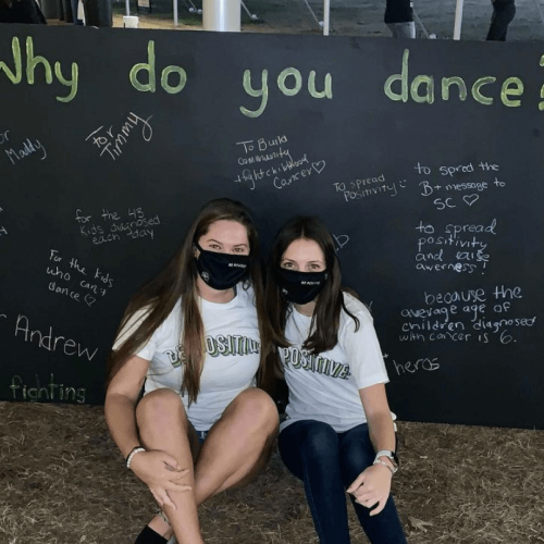 Two students sit in front of a large chalkboard about the Dance Marathon