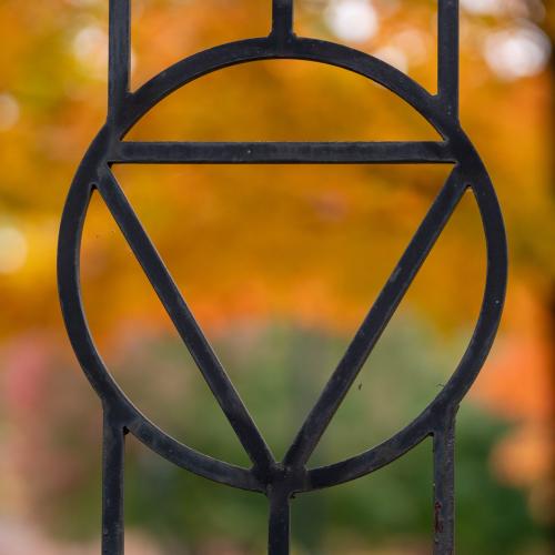 Gulick triangle in fence on campus with autumn leaves.