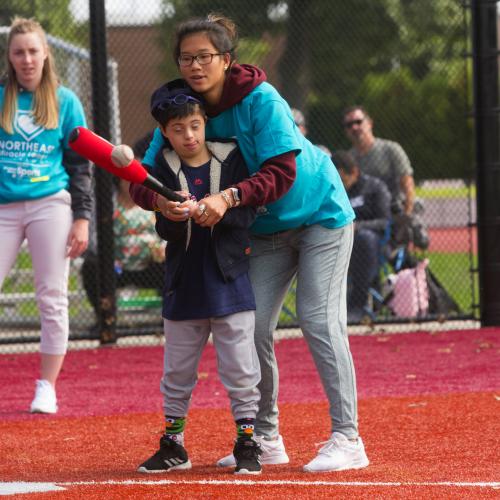 Miracle league student helping child with baseball bat