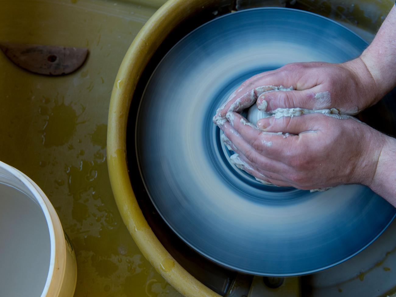 A pair of hands sculpting a clay bowl in the art studio.