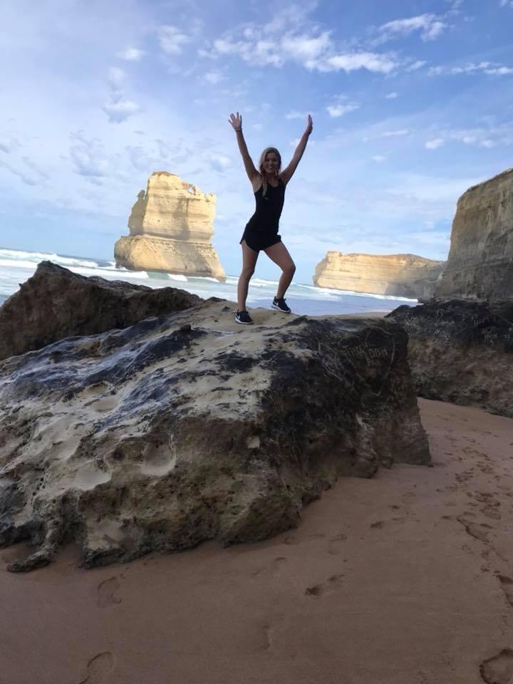 Meghan Godfrey stands on a large rock by the ocean. 
