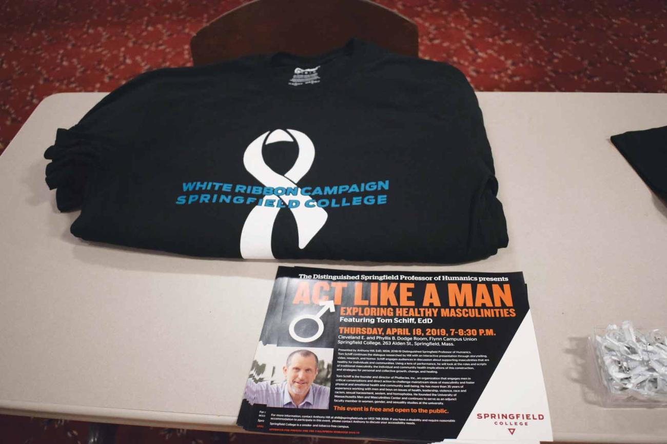 White Ribbon Campaign T-shirt on a table with flyer promoting Act Like a Man presentation