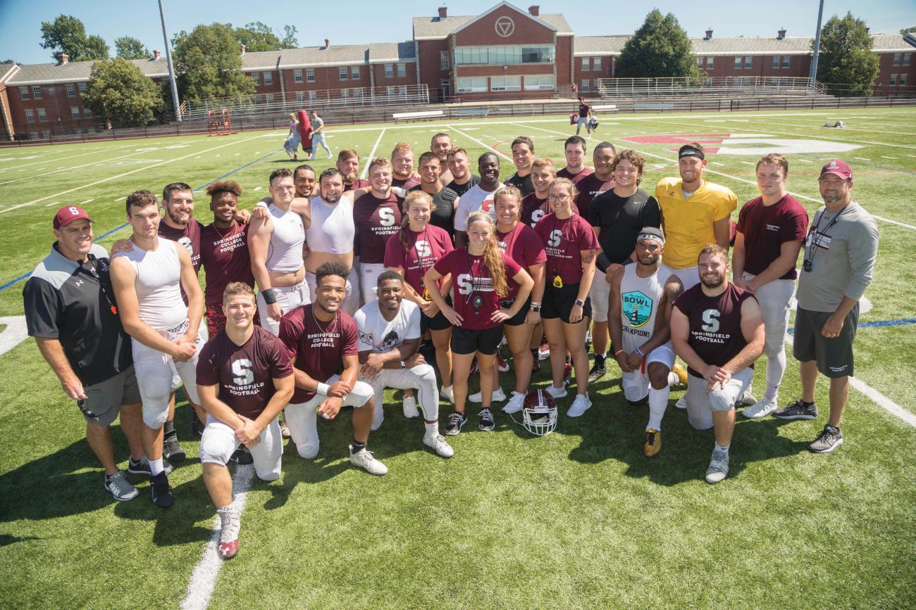 Springfield College Football strength and conditioning coaches at center from left, Izabella Mocarski, Kellie Gambell, Olivia Indorf, and Terrie Bradshaw with players and coaching staff