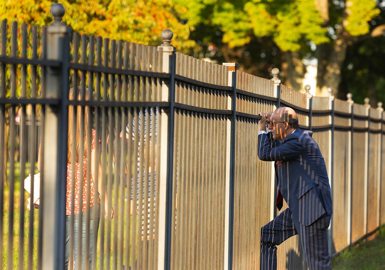 Craig Poisson looks through a fence at an athletic competition