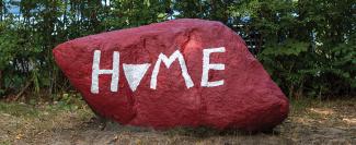  a rock paintd maroon with the word Home on it in white