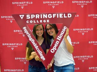 Two female students pose in a triangle cut out during open house.