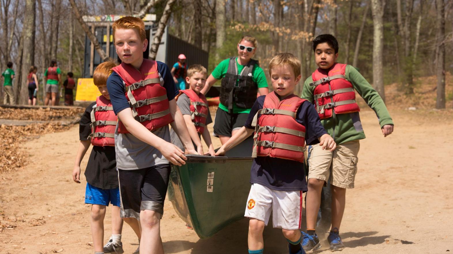 Students carry at canoe down to Watershops Pond as part of Spring Explorers