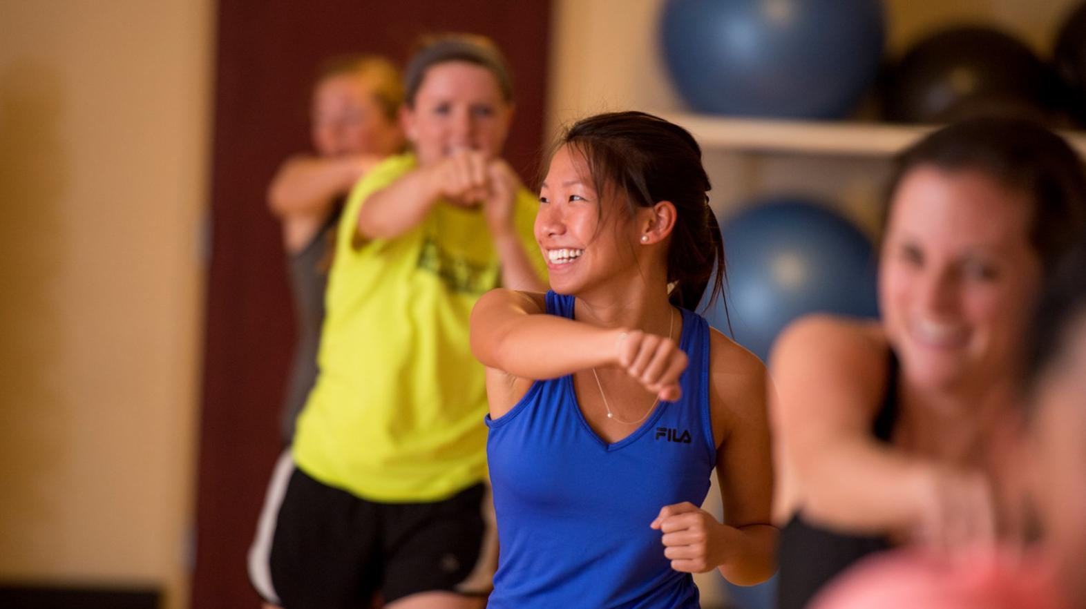 Female students smile as they work out in a group exercise class at Springfield College