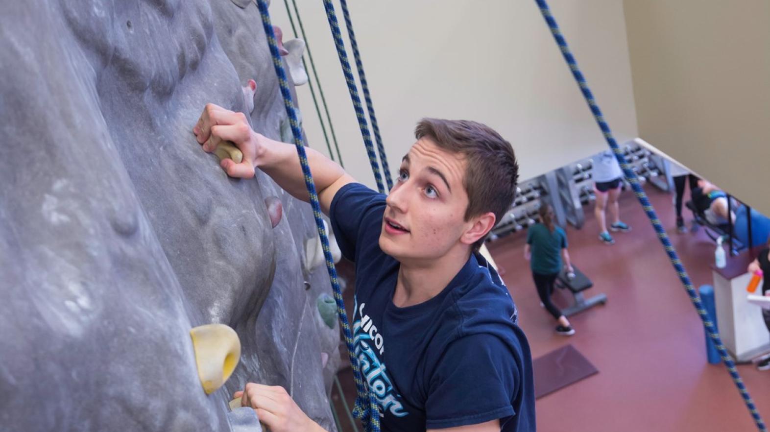 Male student using the climbing wall in Springfield College Wellness Center