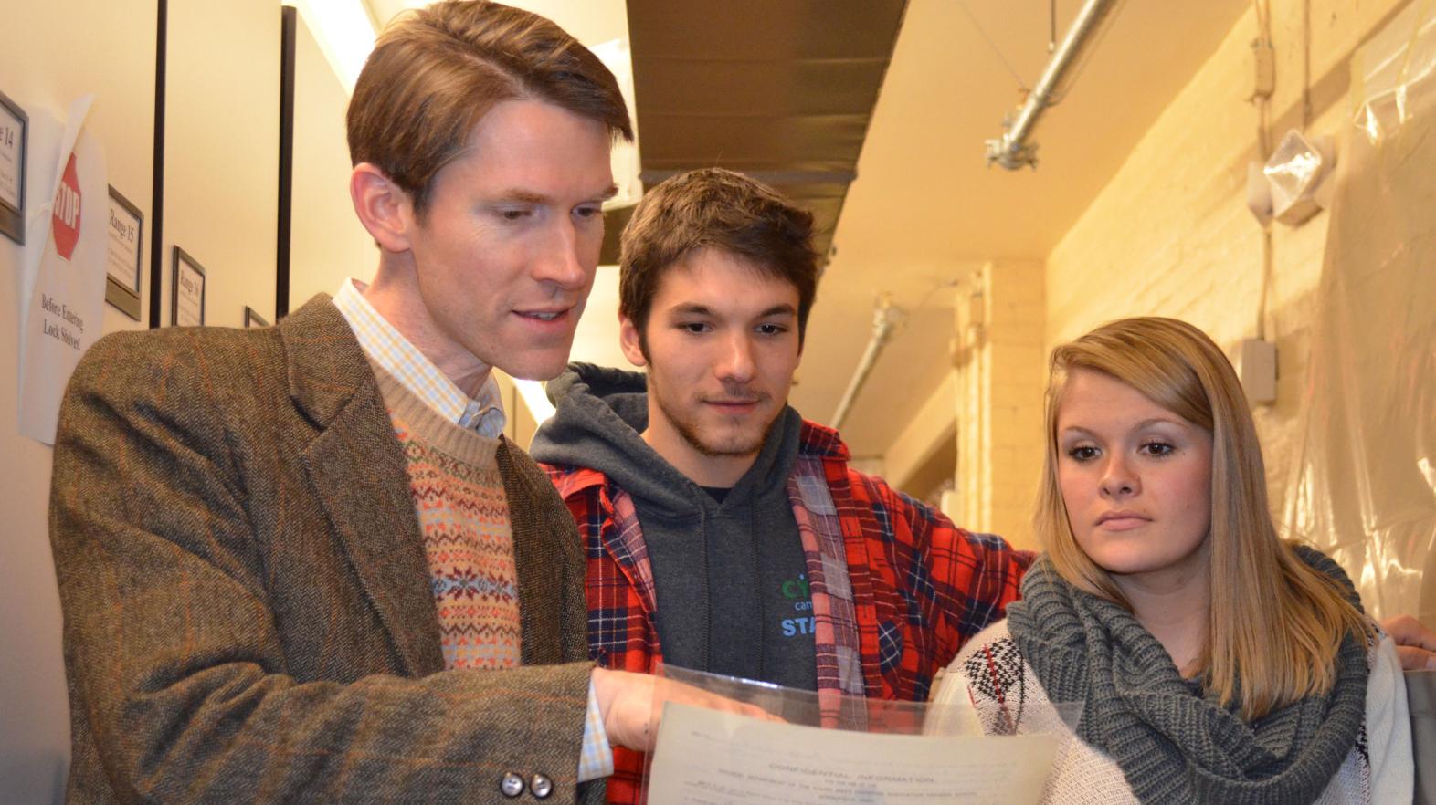 Professor Tom Carty looks at James Naismith's Springfield College application with two students.