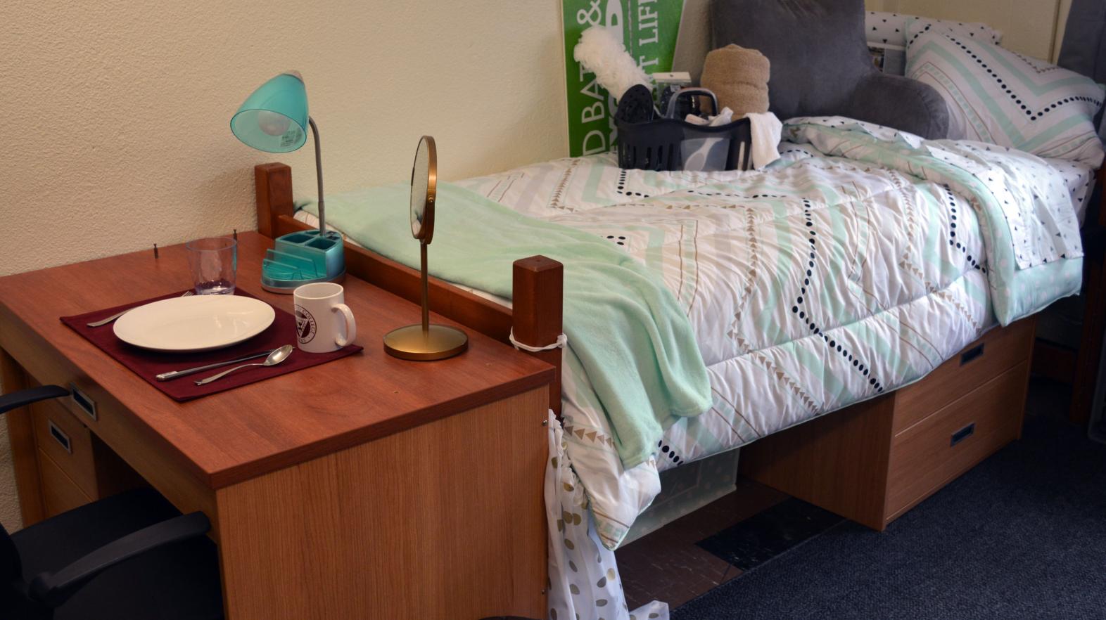 A desk with a plate on it and a bed in Massasoit Hall.