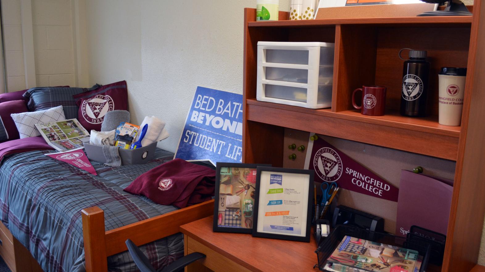 A Massasoit Hall residence room with bed and desk adorned with Springfield College gear.
