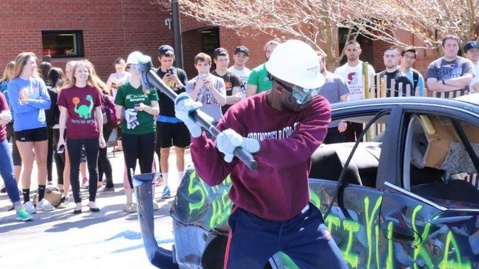 A student swings a hammer at a car as part of the whack-a-car event at Sti-Yu-Ka