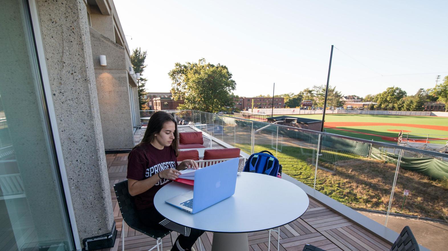 A female student works on her laptop outdoors on the Cooper Terrace of the Learning Commons.