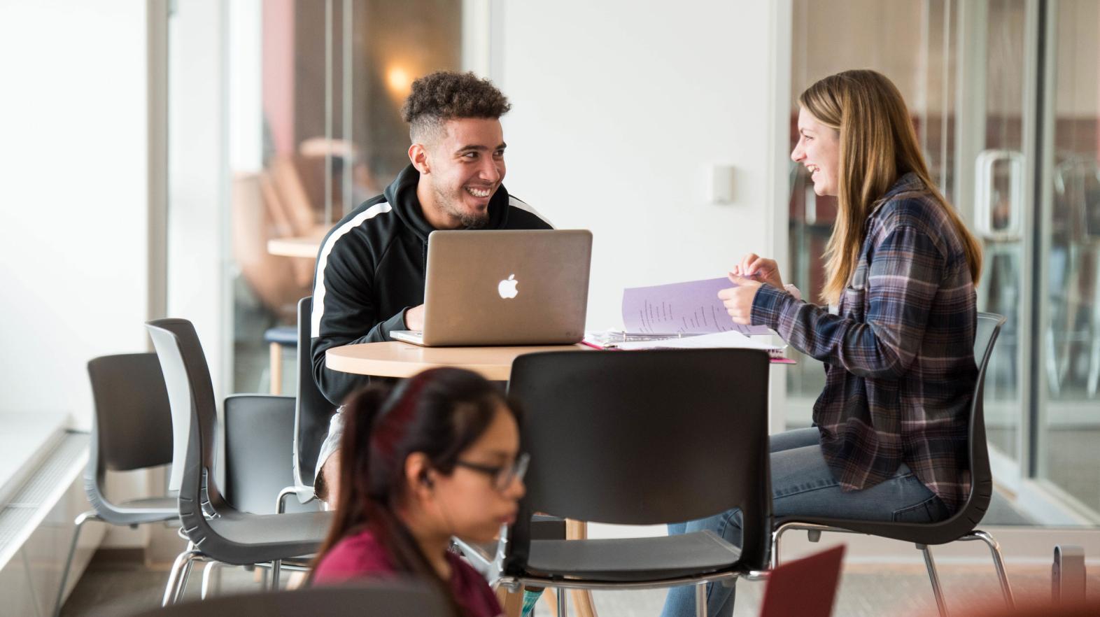 A male and female student talk at a table in the Learning Commons.