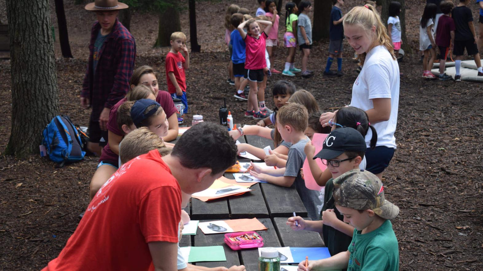 Campers sit at a long table working on crafts.